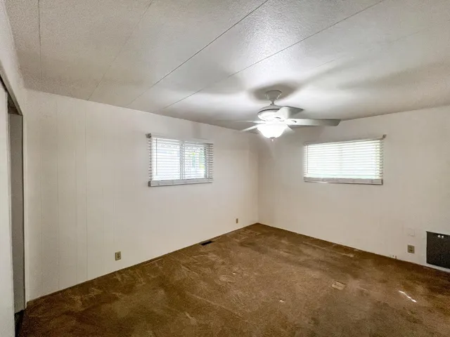 an empty room with a chandelier fan and windows