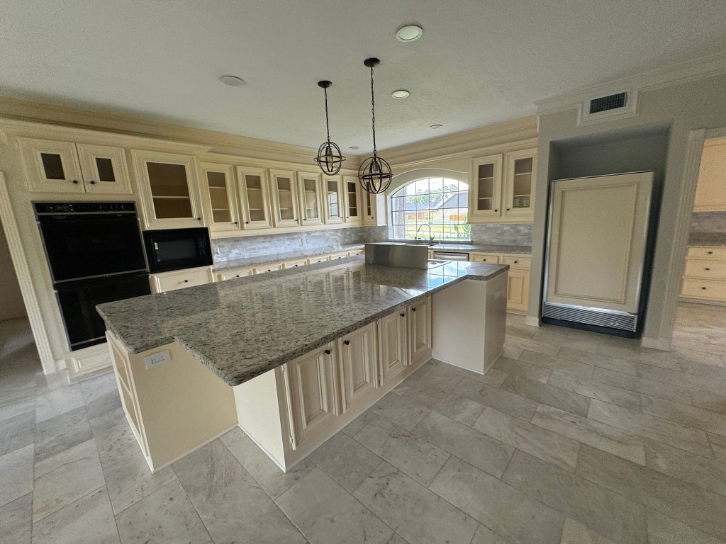 27165 Kestrel Trail Magnolia, TX 77354 - Photo 12 of 50 This spacious kitchen features a large granite island, ample cabinetry, and modern appliances. The room is brightened by an arched window, and elegant pendant lighting adds a stylish touch.