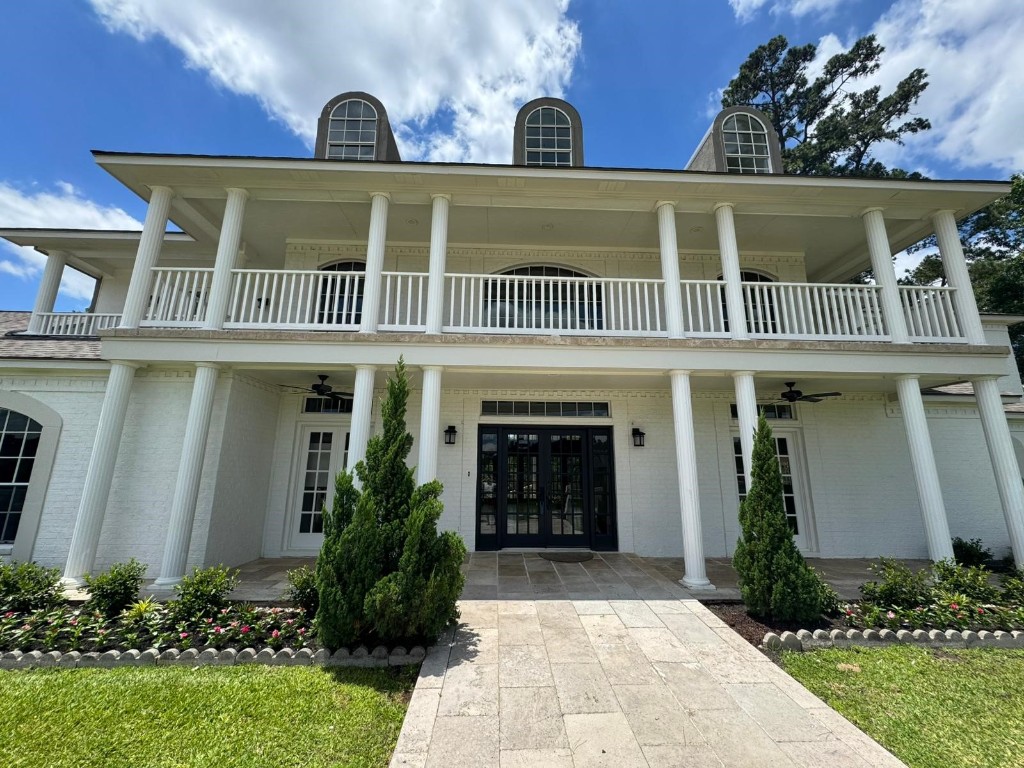 27165 Kestrel Trail Magnolia, TX 77354 - Photo 2 of 50 This photo showcases a classic two-story home with a grand facade, featuring a wide balcony supported by elegant columns. The exterior is painted white, with landscaped greenery and a stone pathway leading to the entrance.