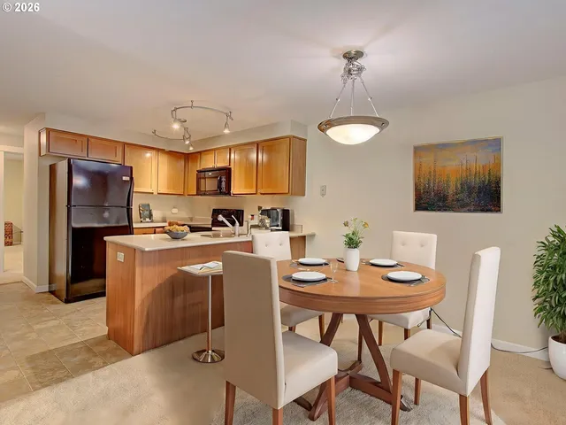 a kitchen with stainless steel appliances granite countertop a dining table chairs refrigerator and microwave