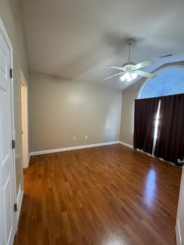 an empty room with wooden floor fan and window
