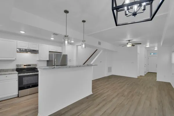 a open kitchen with stainless steel appliances kitchen island a refrigerator wooden floor and a ceiling fan