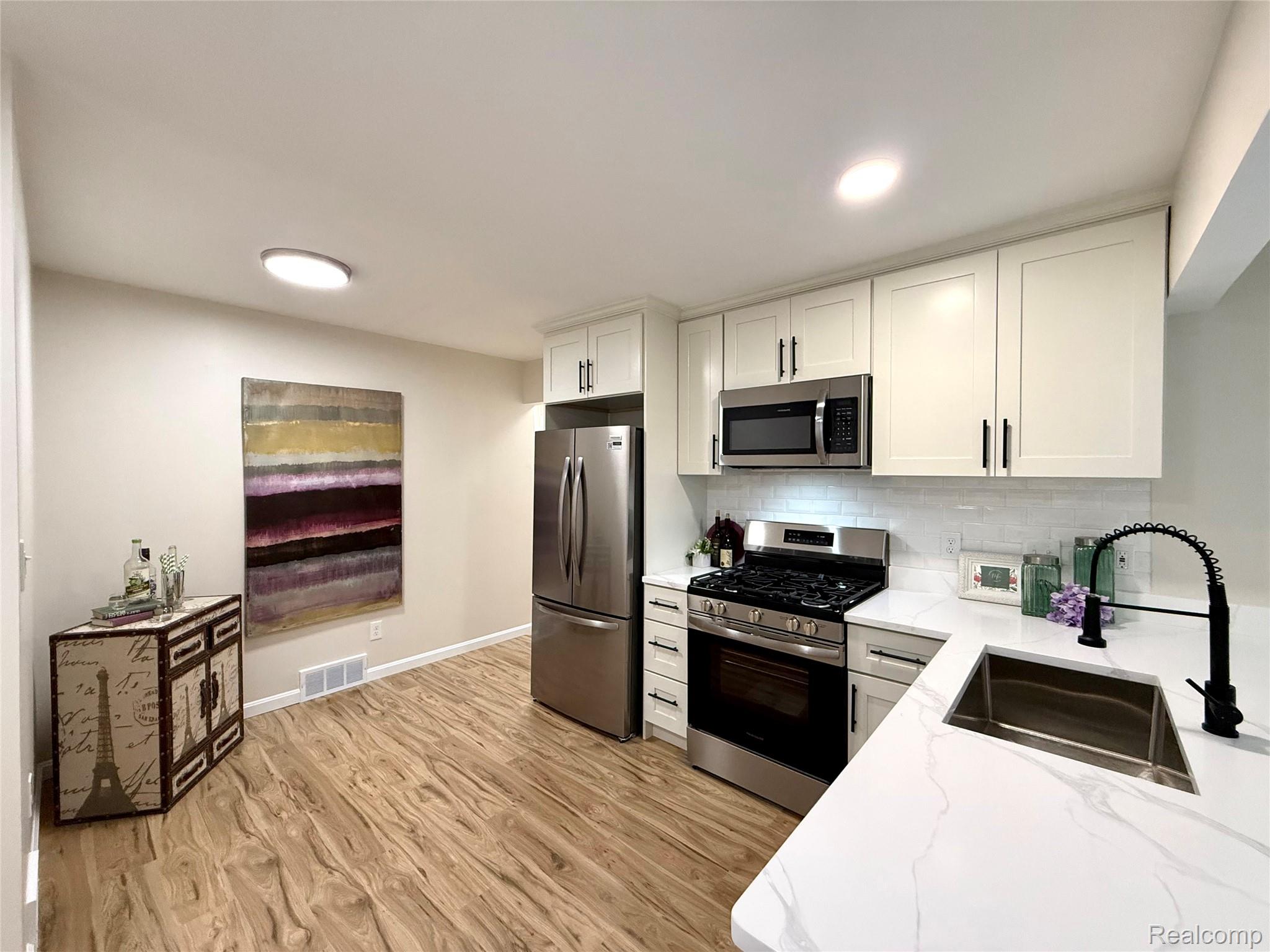 39909 Lynn Street Canton, MI 48187 - Photo 6 of 45 Modern kitchen featuring light wood-finish flooring, white cabinetry, stainless steel appliances, white subway tile backsplash, and white countertops