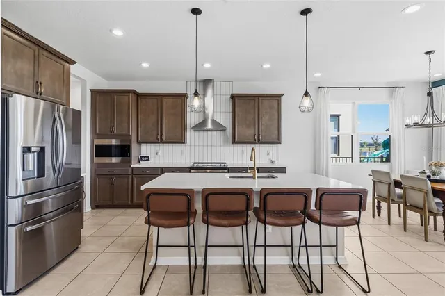 a kitchen with stainless steel appliances a sink a stove a refrigerator cabinets and chairs