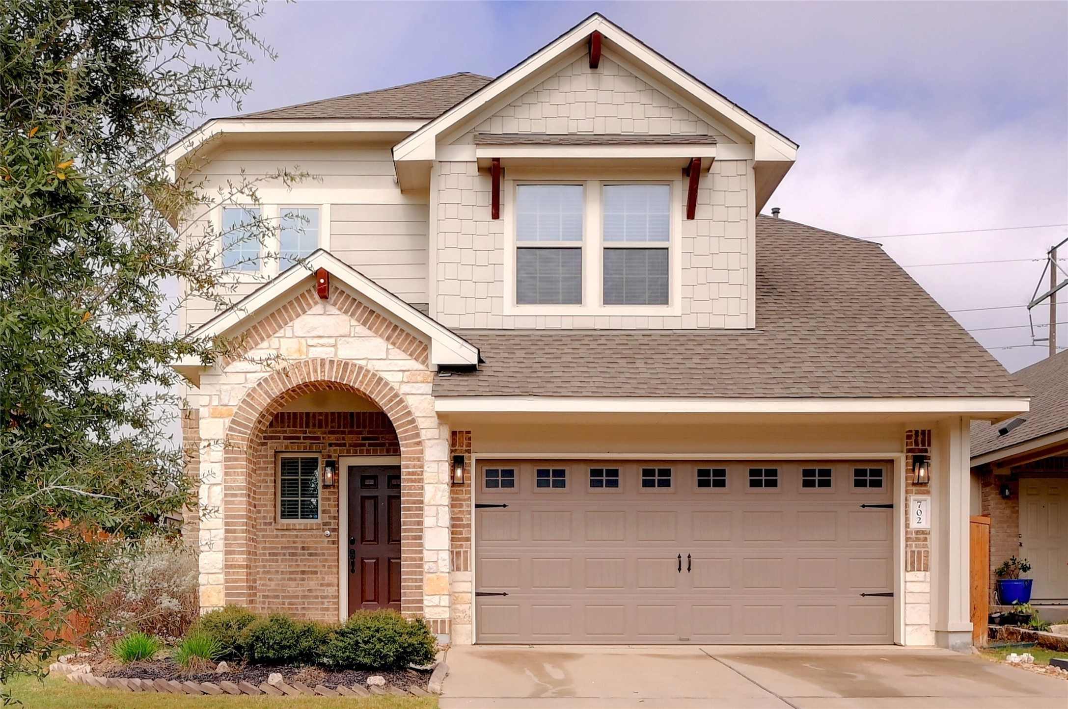 The property features a charming exterior with brick and stone accents, a covered arched entryway, and a two-car garage