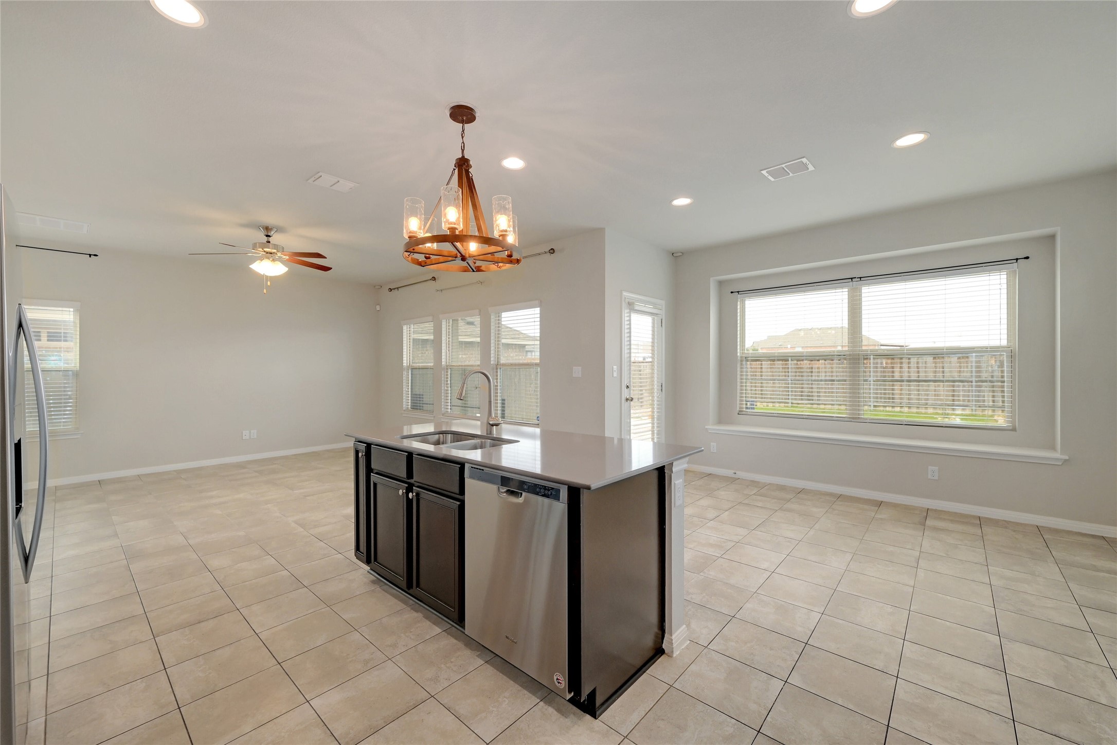 702 Nautical Loop Kyle, TX 78640 - Photo 11 of 27 The open concept living area features tile flooring, a kitchen island with a sink and stainless steel dishwasher, and a decorative chandelier