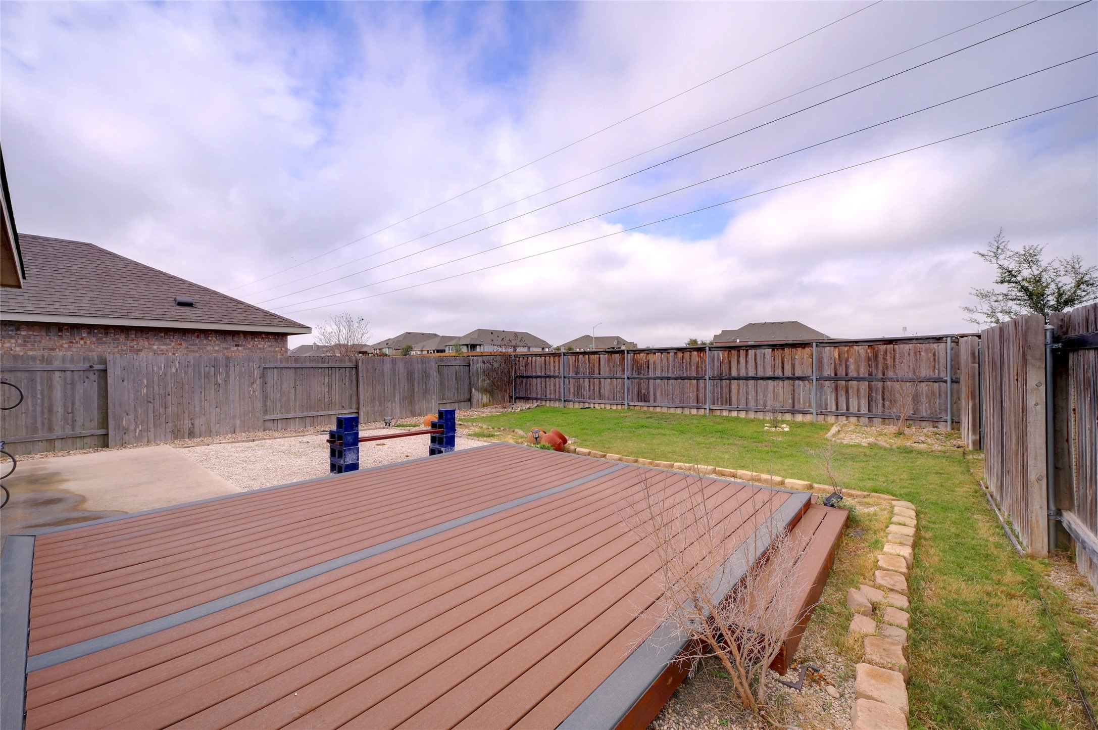 702 Nautical Loop Kyle, TX 78640 - Photo 26 of 27 The property features a fenced backyard with a spacious deck, a lawn area, and a gravel section
