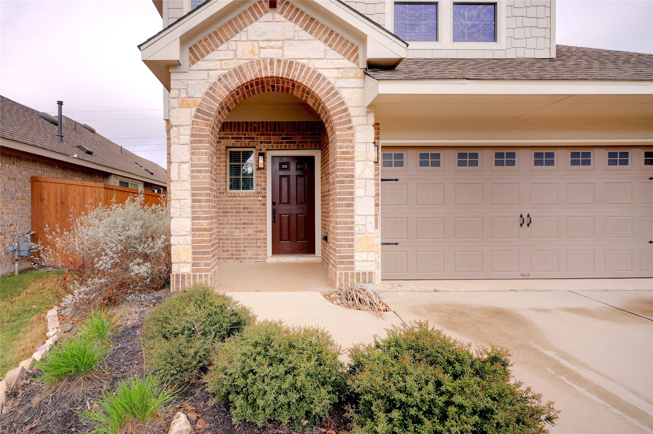 702 Nautical Loop Kyle, TX 78640 - Photo 3 of 27 The property features an arched stone and brick entryway, a dark wood front door, and a two-car garage with decorative hardware and windows