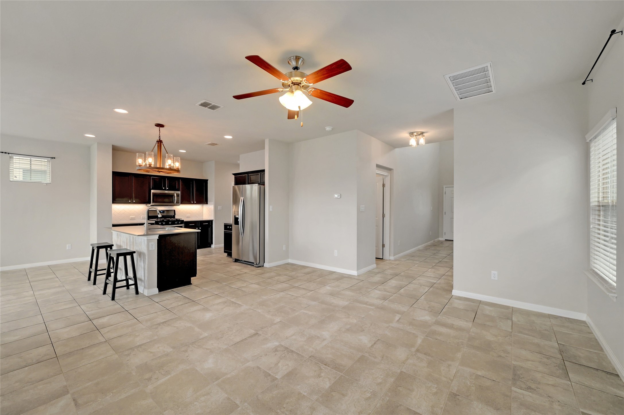 702 Nautical Loop Kyle, TX 78640 - Photo 5 of 27 This open-concept living area features light-colored tile flooring throughout, a kitchen island with seating, dark wood cabinetry, and stainless steel appliances