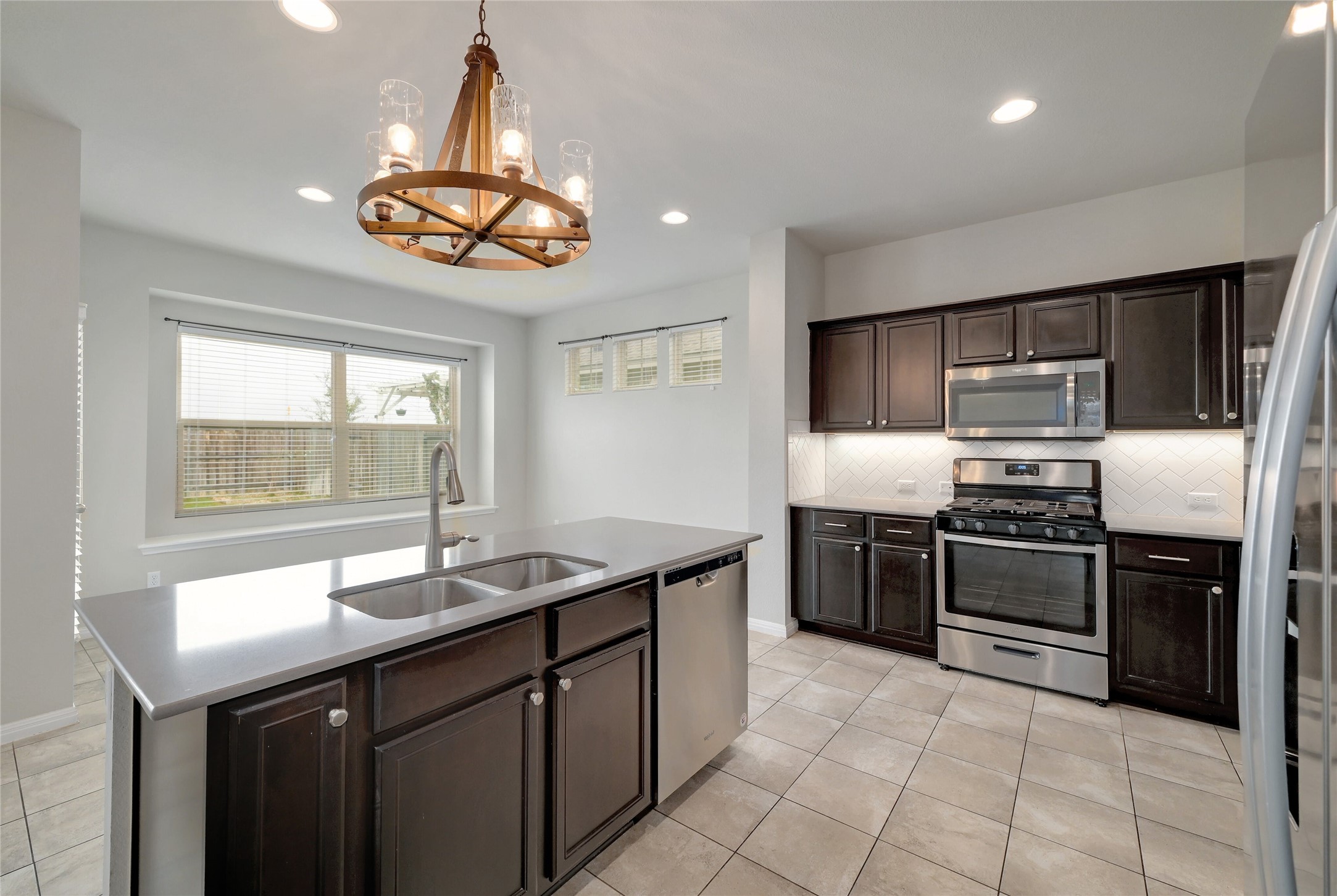 702 Nautical Loop Kyle, TX 78640 - Photo 8 of 27 The kitchen features a large island with a double sink, dark wood cabinetry, stainless steel appliances, and a tiled floor