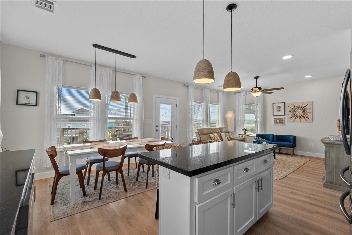 130 Beachcomber Avenue Surfside Beach, TX 77541 - Photo 13 of 33 Bright, open-concept living space featuring modern kitchen with island, adjacent dining area with large windows, and cozy seating area. Neutral tones and wood look flooring enhance the airy feel.
