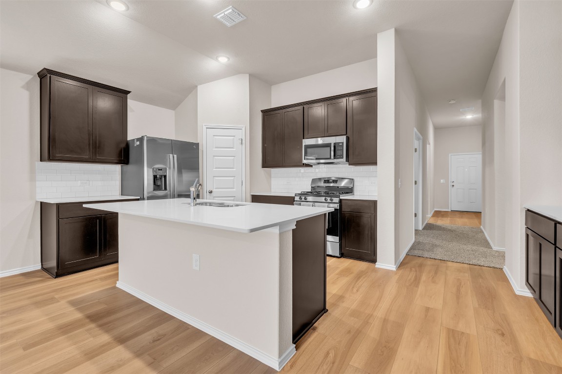 9200 Furman Drive Austin, TX 78747 - Photo 2 of 15 Kitchen featuring tasteful backsplash, dark brown cabinetry, appliances with stainless steel finishes, and light wood-type flooring