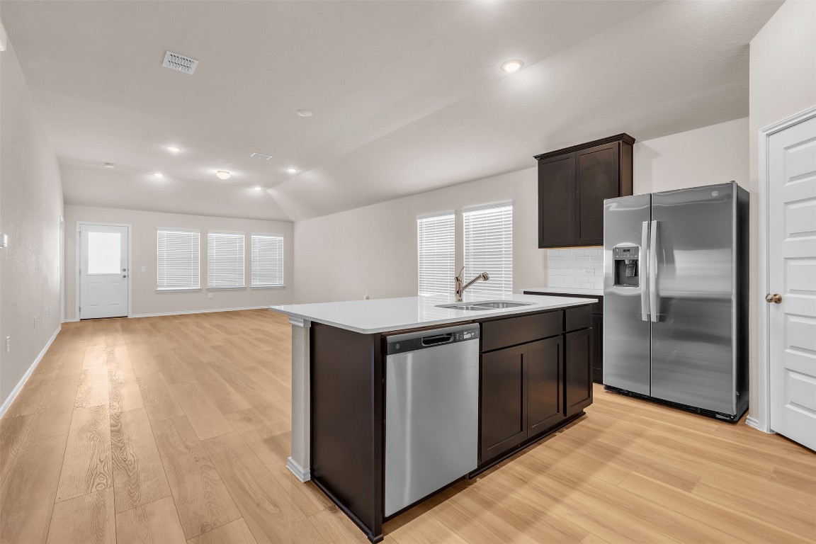 9200 Furman Drive Austin, TX 78747 - Photo 15 of 15 Kitchen featuring appliances with stainless steel finishes, a kitchen island with sink, light wood-style floors, open floor plan, and decorative backsplash