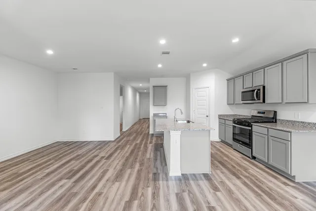 a large kitchen with kitchen island a stove a sink dishwasher a refrigerator and white cabinets with wooden floor