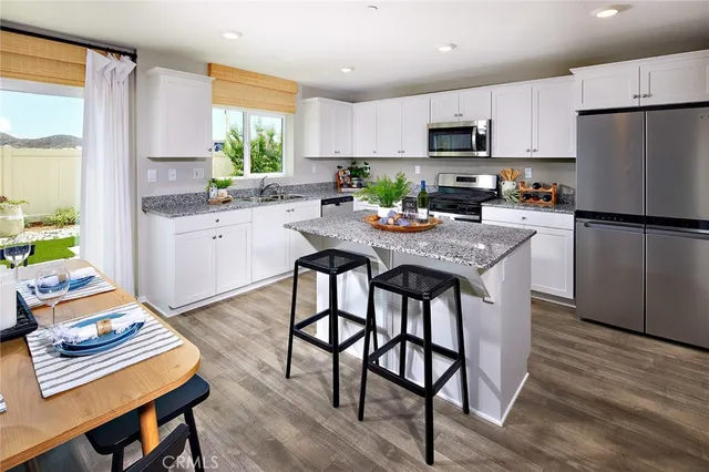 a kitchen with stainless steel appliances granite countertop a refrigerator a stove a sink a dining table and chairs with wooden floor