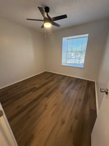 an empty room with wooden floor fan and windows
