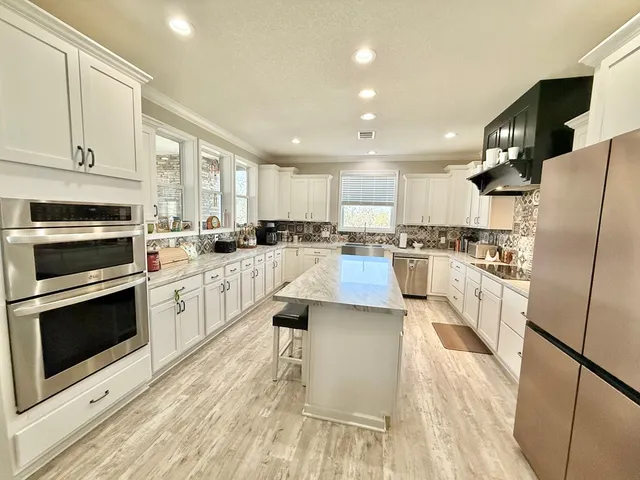 a kitchen with stainless steel appliances kitchen island granite countertop a refrigerator a stove top oven a sink dishwasher and white cabinets with wooden floor