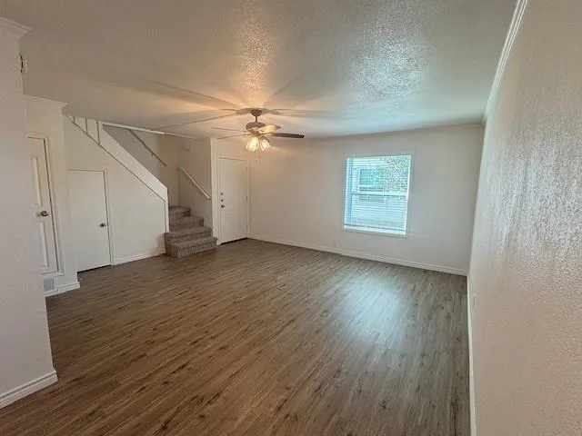 an empty room with wooden floor chandelier fan and windows