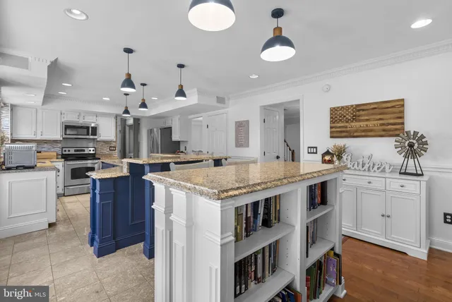 a kitchen with kitchen island granite countertop a stove top oven a sink dishwasher and white cabinets with wooden floor