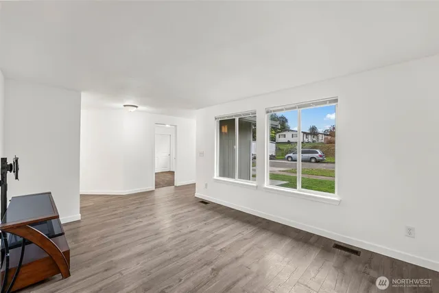 a view of an empty room with wooden floor and a window