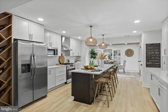 a kitchen with stainless steel appliances kitchen island granite countertop a refrigerator a oven a sink and a dining table with wooden floor