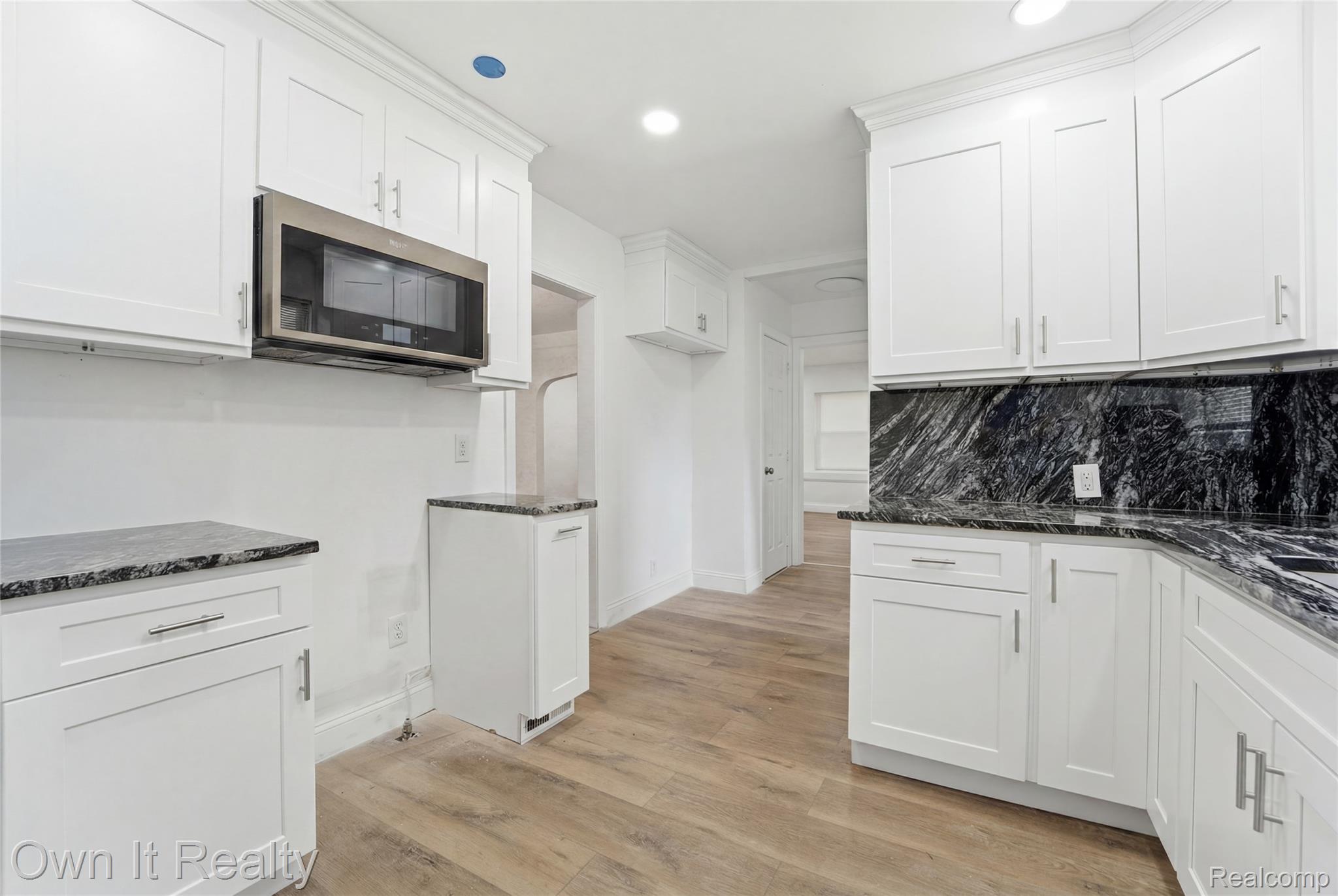 17351 Appoline Street Detroit, MI 48235 - Photo 12 of 34 Contemporary kitchen featuring white shaker cabinetry, stainless steel microwave, black patterned countertops, matching backsplash, and wood-finish flooring