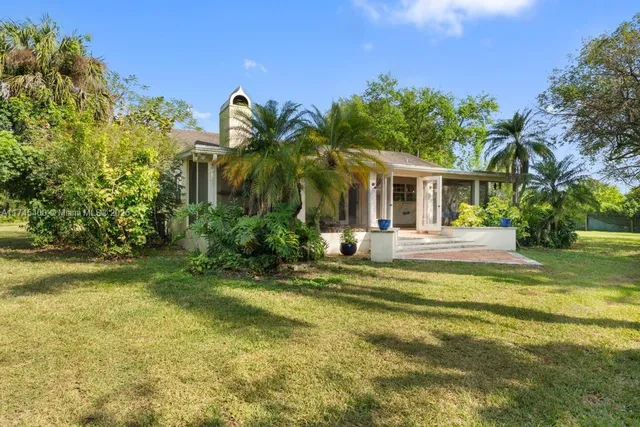 a view of a white house with a big yard and potted plants and large trees
