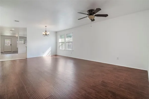 an empty room with wooden floor chandelier fan and windows
