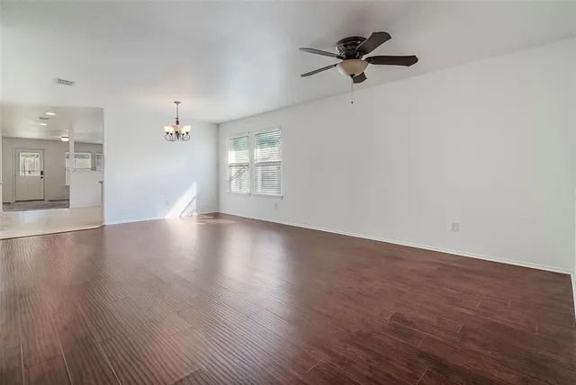 an empty room with wooden floor chandelier fan and windows