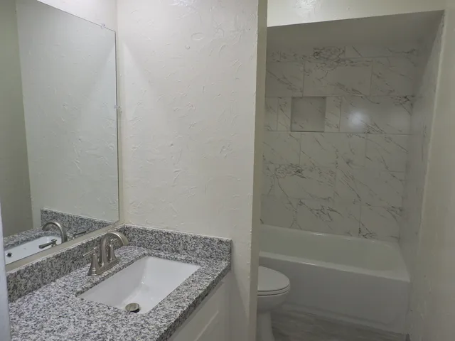 a bathroom with a granite countertop sink a toilet and bathtub