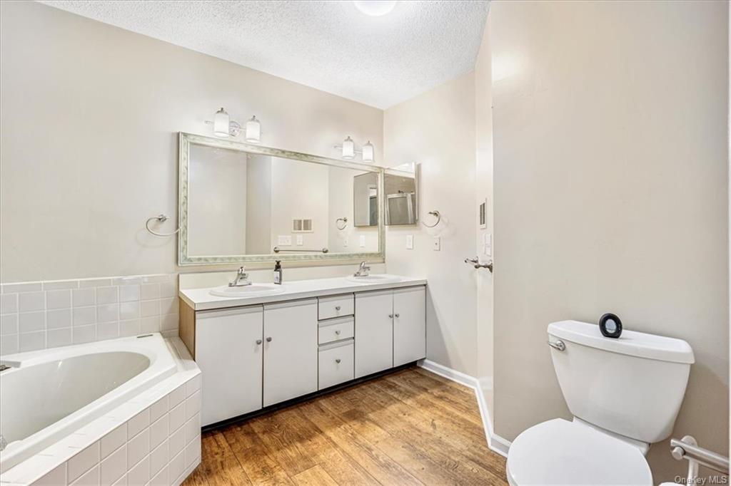 1 Chadwick Court Fishkill, NY 12524 - Photo 22 of 35 Bathroom with a relaxing tiled tub, a textured ceiling, hardwood / wood-style floors, vanity, and toilet