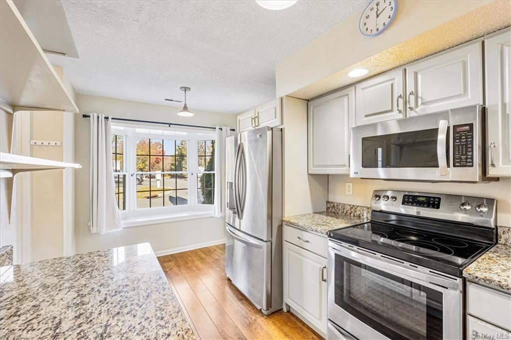 1 Chadwick Court Fishkill, NY 12524 - Photo 7 of 35 Kitchen featuring white cabinetry, appliances with stainless steel finishes, a textured ceiling, light stone countertops, and light hardwood / wood-style flooring