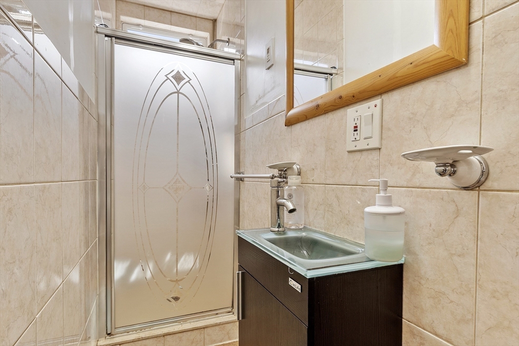 483 Broadway, Unit 1 Medford, MA 02155 - Photo 9 of 13 a bathroom with a granite countertop sink a mirror and shower