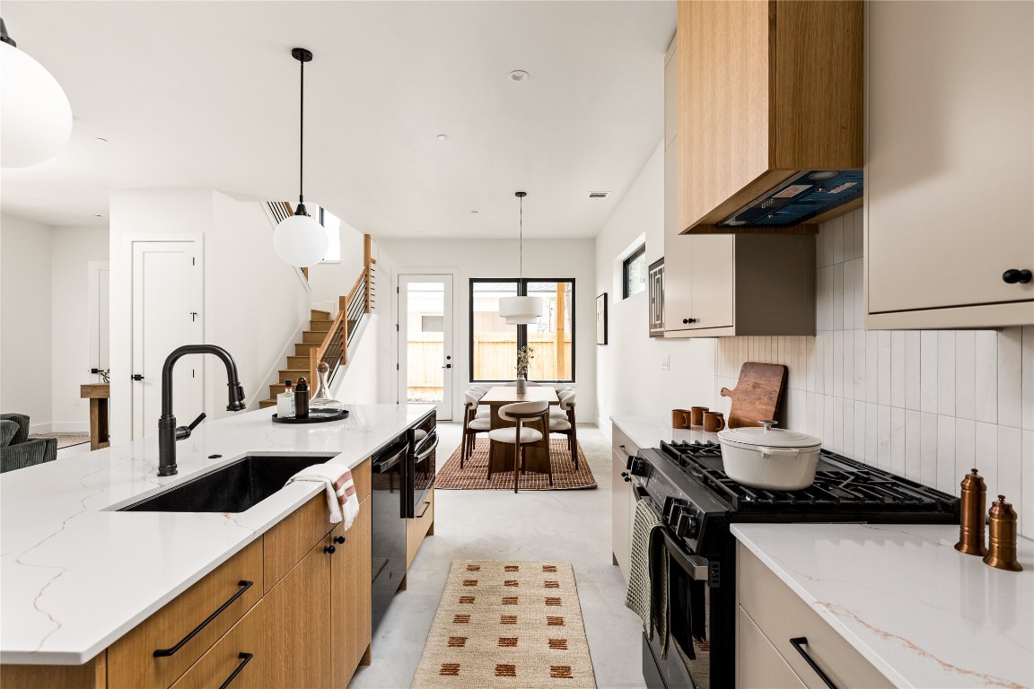 4416 South 1st Street, Unit 2 Austin, TX 78745 - Photo 14 of 40 Kitchen with black appliances, decorative light fixtures, light stone counters, custom exhaust hood, and a center island with sink