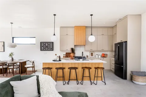 a kitchen with stainless steel appliances kitchen island granite countertop a sink a refrigerator a stove a dining table and chairs with wooden floor