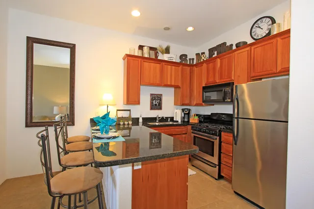 a kitchen with stainless steel appliances granite countertop a refrigerator a stove a sink a dining table and chairs with wooden floor