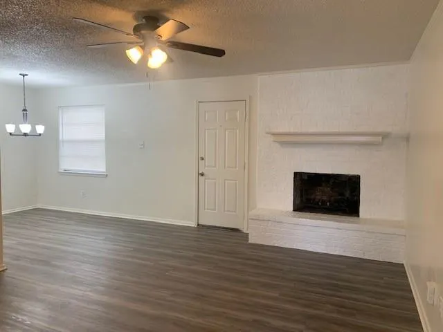 an empty room with wooden floor a ceiling fan a fireplace and windows