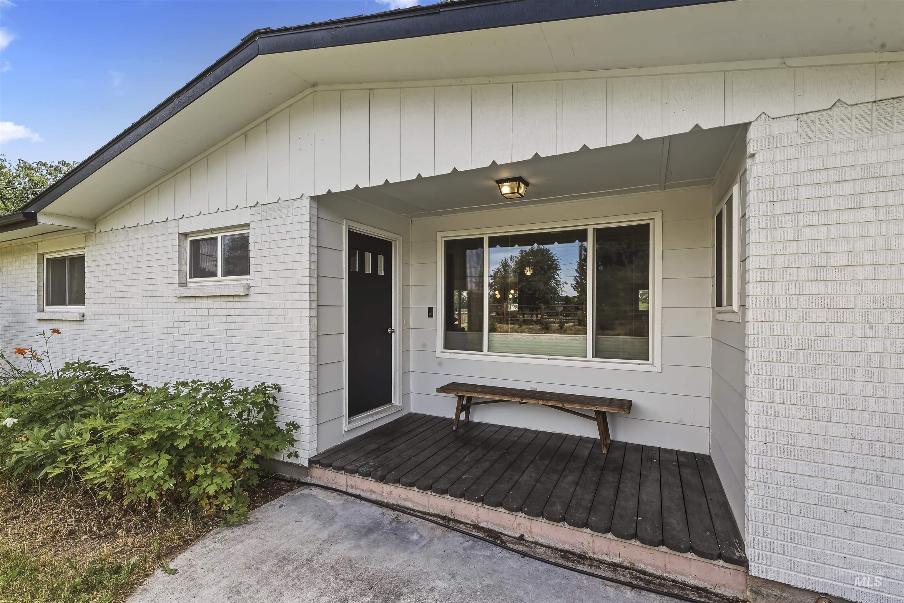 355 East Beacon Light Road Eagle, ID 83616 - Photo 3 of 47 White painted brick exterior with a black entry door featuring vertical glass inserts, a covered wood-plank porch, and a bronze outdoor ceiling fixture