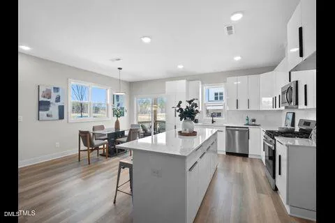 a large white kitchen with stainless steel appliances granite countertop a stove oven a sink dishwasher a dining table and chairs with wooden floor