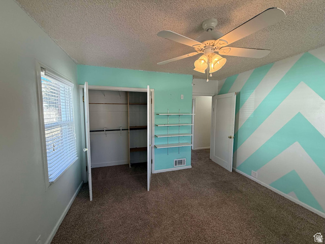 73 Garden Street Helper, UT 84526 - Photo 30 of 36 Unfurnished bedroom with dark carpet, ceiling fan, a closet, a textured ceiling, and an accent wall