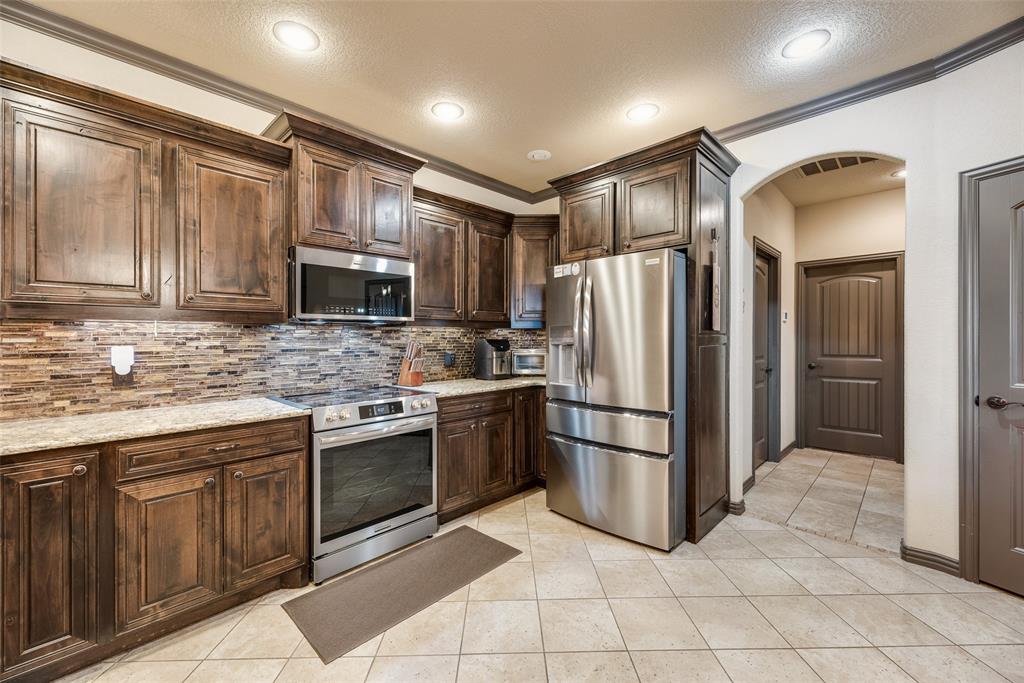 1132 Chartres Street Kaufman, TX 75142 - Photo 8 of 25 Modern kitchen with stainless steel appliances, rich wood cabinetry, patterned tile backsplash, and light-toned tile flooring