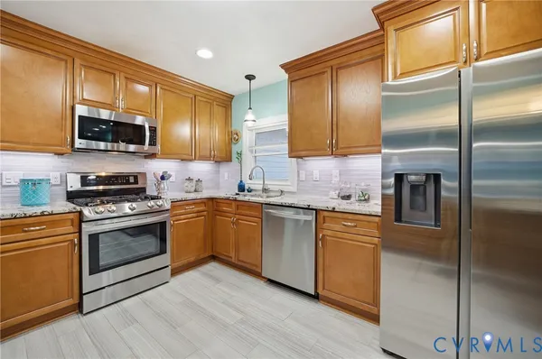 a kitchen with stainless steel appliances granite countertop a refrigerator a sink dishwasher a stove and a large countertops with wooden floor