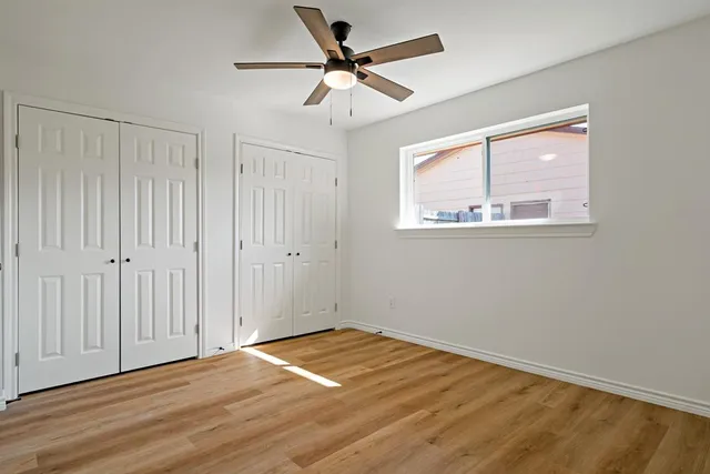 an empty room with wooden floor fan and windows