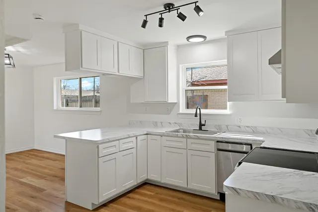 a kitchen with a sink dishwasher a stove and white cabinets with wooden floor