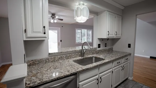 a kitchen with stainless steel appliances granite countertop a sink dishwasher and white cabinets with wooden floor