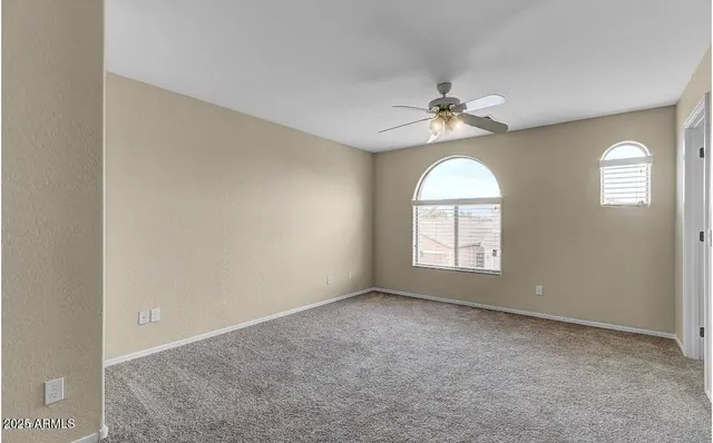 an empty room with a chandelier fan and windows