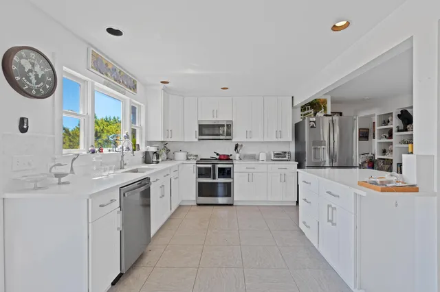 a large white kitchen with a stove top oven a clock and a window
