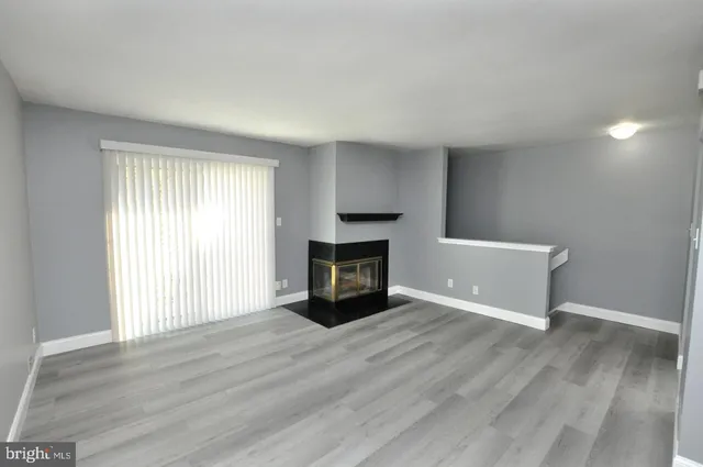 an empty room with wooden floor fireplace and windows