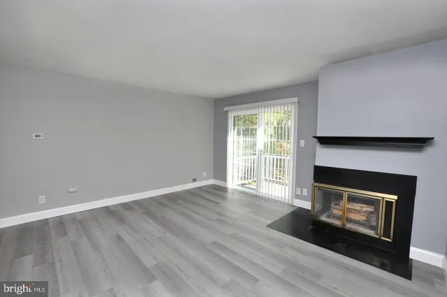 a view of an empty room with wooden floor fireplace and a window