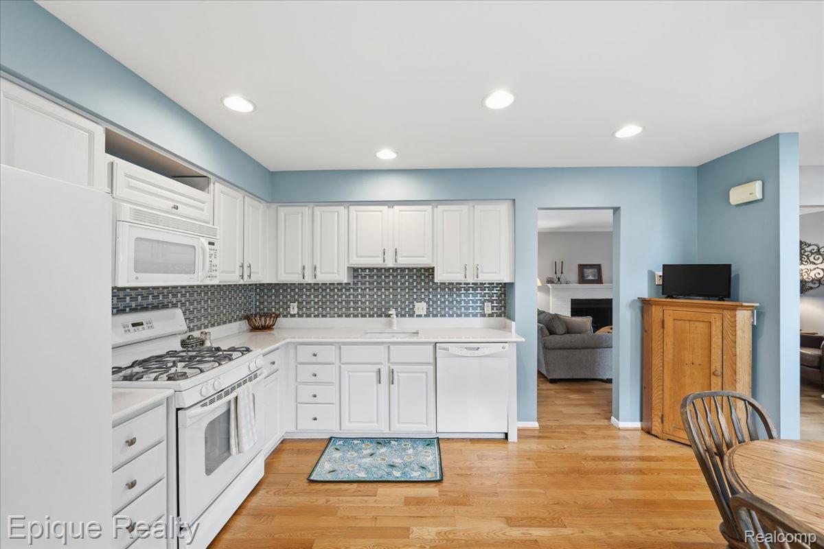 26 Kirks Court Rochester, MI 48309 - Photo 16 of 44 Bright kitchen featuring L-shaped white cabinetry, white appliances, recessed lighting, wood-finish flooring, and a patterned tile backsplash